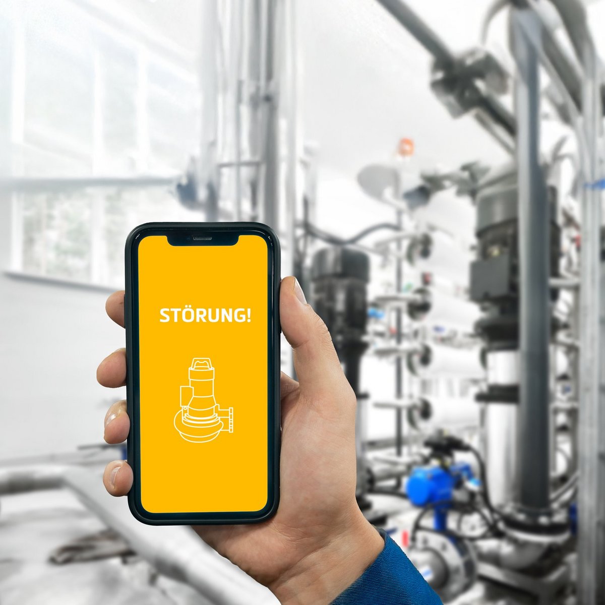 Ein Handwerker hält ein Smartphone mit einer Störungsmeldung in einer modernen Industrieumgebung mit Rohren und Maschinen.
