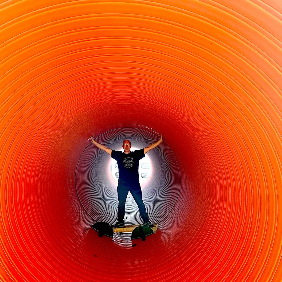 Ein Mann steht in einem großen, orangefarbenen Tunnel und breitet seine Arme aus, während er lächelt.
