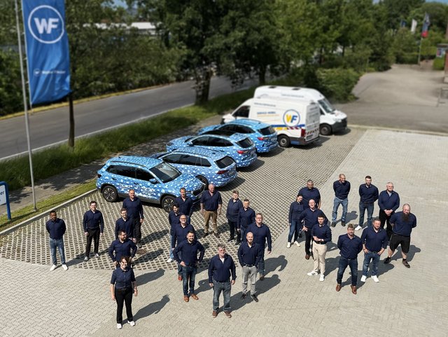 Die Mitarbeitenden von Walter Fiedler stehen auf dem Parkplatz in Form der Zahl 100
