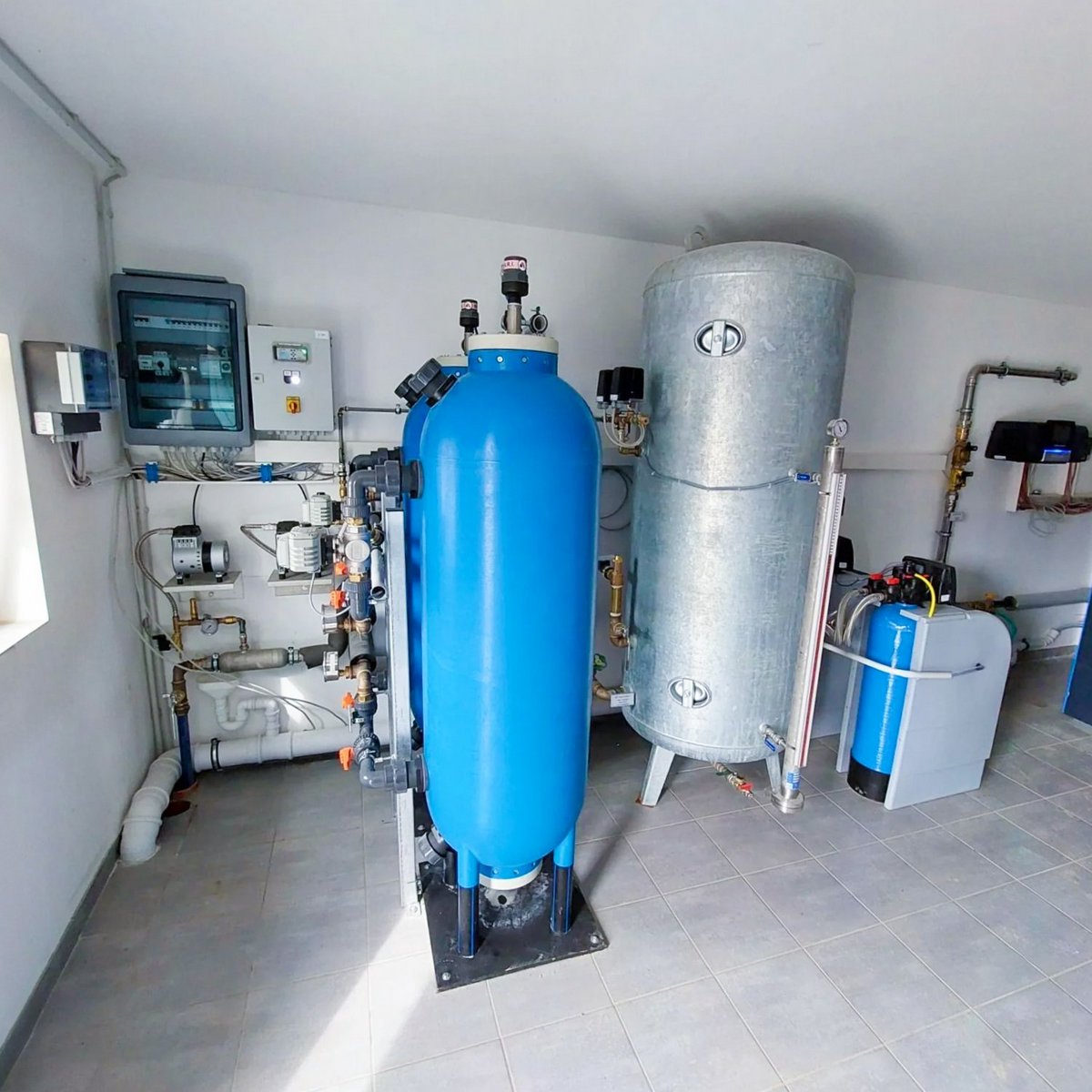 Ein Raum mit verschiedenen Wasseraufbereitungsanlagen, darunter ein großer blauer Tank und ein silberner Wassertank.
